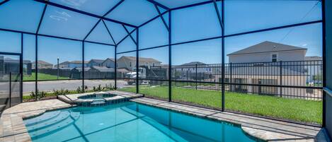 A swimming pool with a glass enclosure, surrounded by a brick patio and a metal fence.
