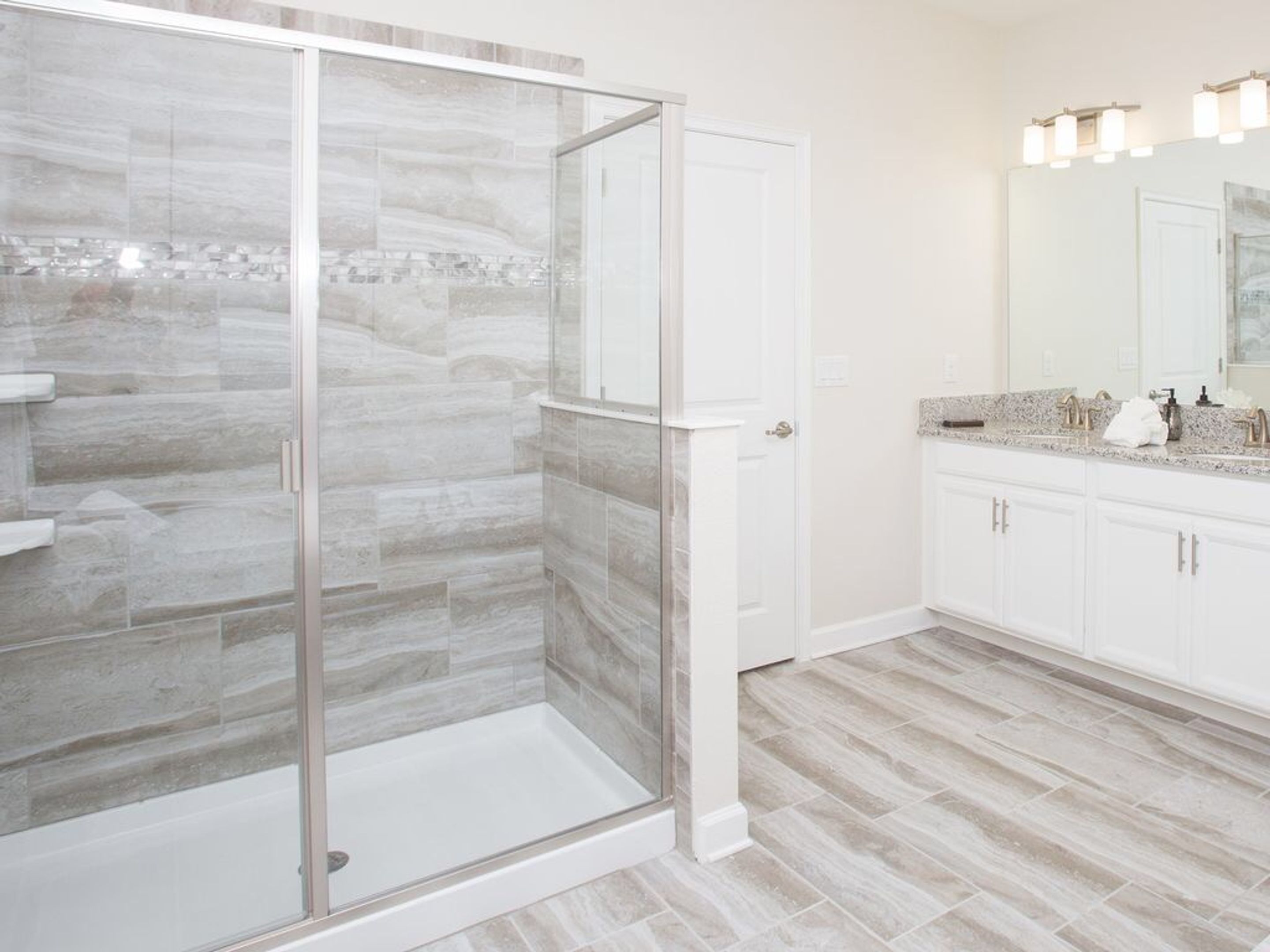A modern bathroom with a glass-enclosed shower, white cabinets, and a granite countertop.