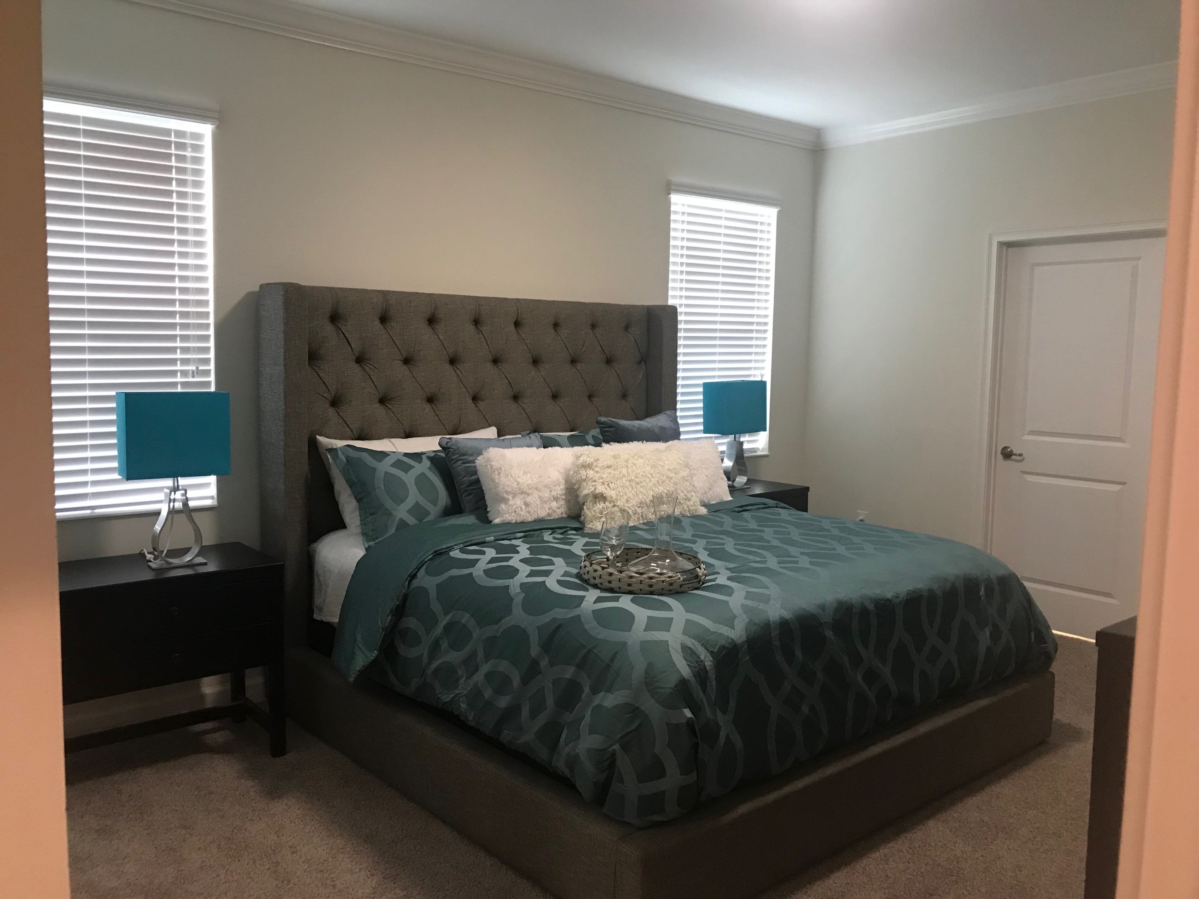 A bedroom with a tufted headboard, a bed with patterned bedding, two bedside tables with lamps, and a door.