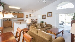 A spacious living area with a sofa, wooden dining table, and chairs. A kitchen with wooden cabinets and a microwave is visible in the background. - High Gate Park 204 (Davenport)