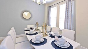 Uma sala de jantar com uma mesa branca posta para quatro pessoas, rodeada por cadeiras brancas.