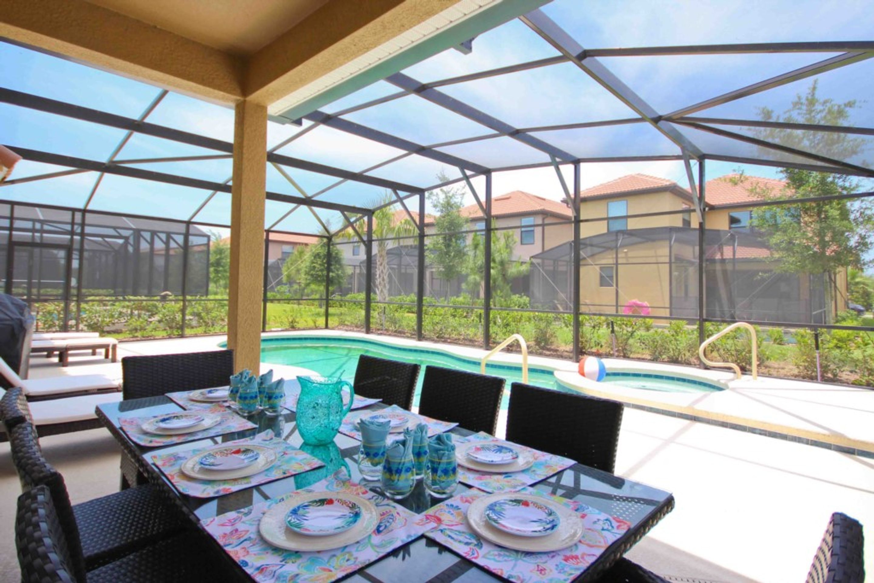 An outdoor patio with a pool, covered seating, and a table set for dining.