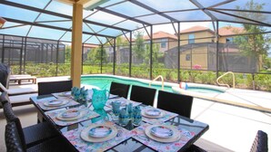 Um pátio externo com piscina, área de estar coberta e mesa posta para refeições.