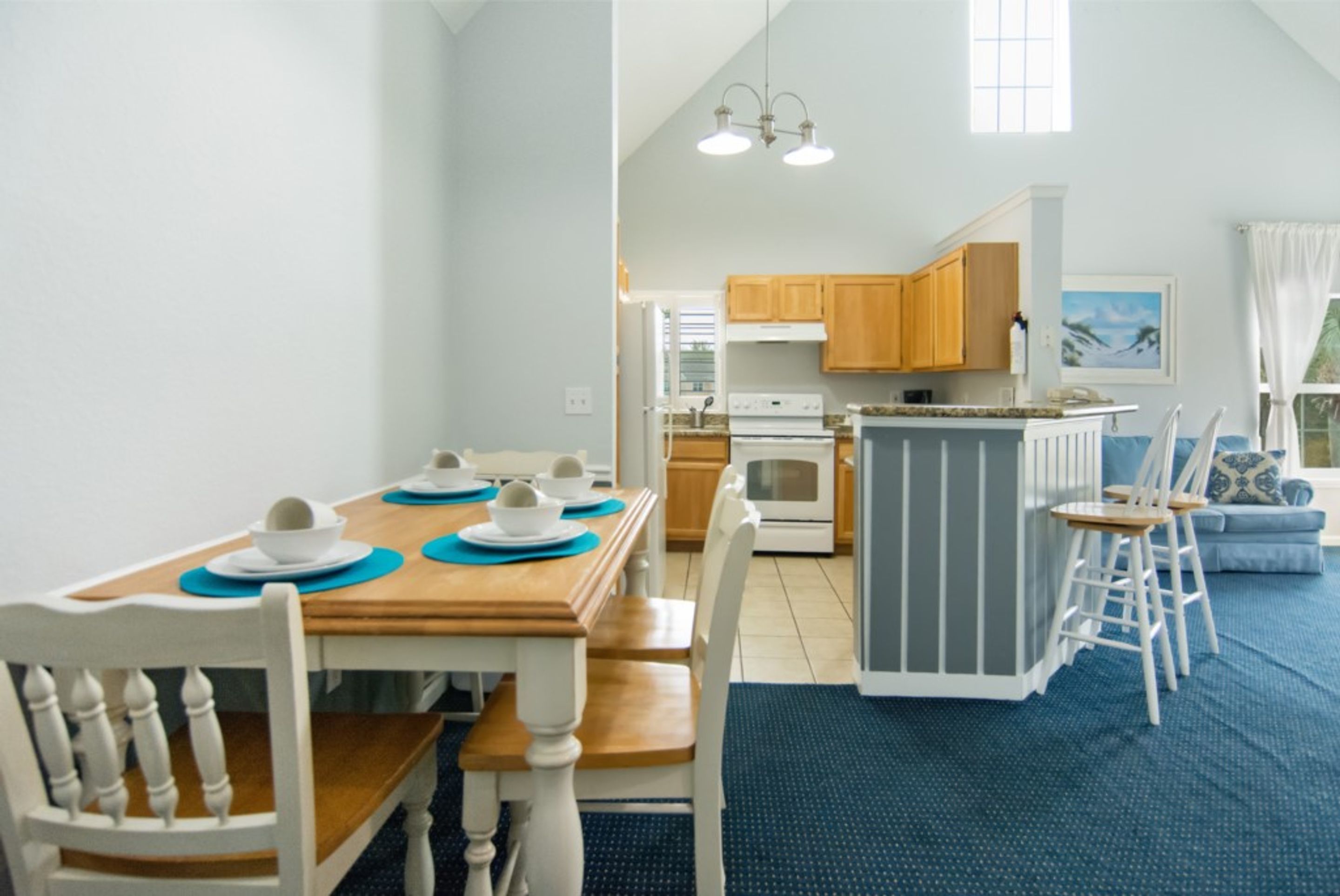 A compact kitchen with wooden cabinets, a central island, and a dining area with a wooden table and white chairs.