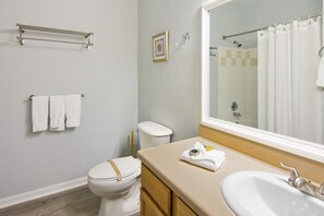 A bathroom with a toilet, a sink, a towel rack, a shower curtain, and a framed picture on the wall. - Runaway Beach 3004 B12.202 (Kissimmee)