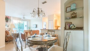 A dining area with a round glass table, chairs, and a chandelier. There is a kitchen in the background with cabinets and a countertop. - Legacy Dunes 8910 B16.208 (Kissimmee)