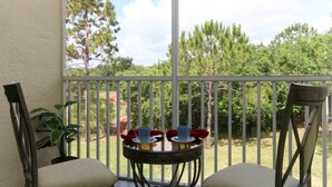 A balcony with two chairs, a small round table with cups and saucers, and a potted plant. - Legacy Dunes 8910 B16.208 (Kissimmee)