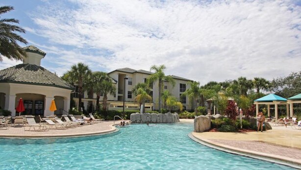 A swimming pool with lounge chairs and umbrellas, surrounded by buildings and palm trees. - Legacy Dunes 8910 B16.208 (Kissimmee)