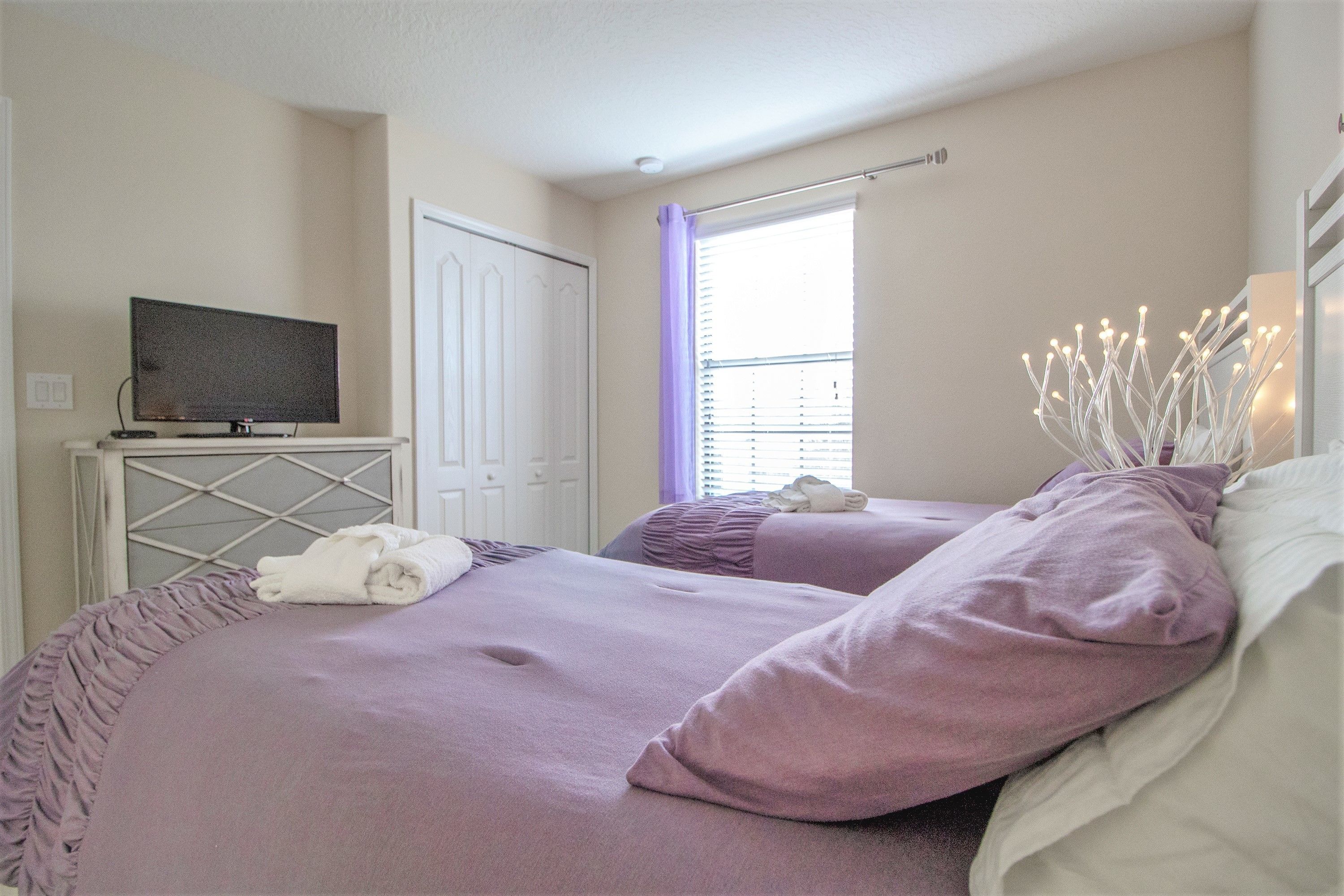 A bedroom with two beds, a television on a stand, and a window with blinds.