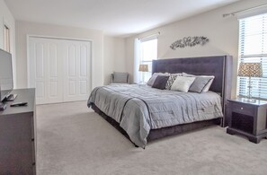 A bedroom with a large bed, a dresser, a TV, and a door. - Champions Gate 9033 (Davenport)