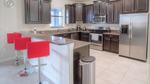 A modern kitchen with dark cabinets, stainless steel appliances, and red bar stools. - Champions Gate 9033 (Davenport)