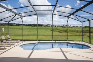 A covered swimming pool with a view of a green field and houses in the background.