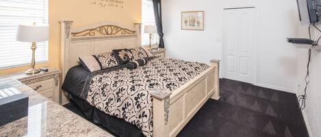 A bedroom with a bed, nightstands, a desk, a ceiling fan, a TV, and a door.