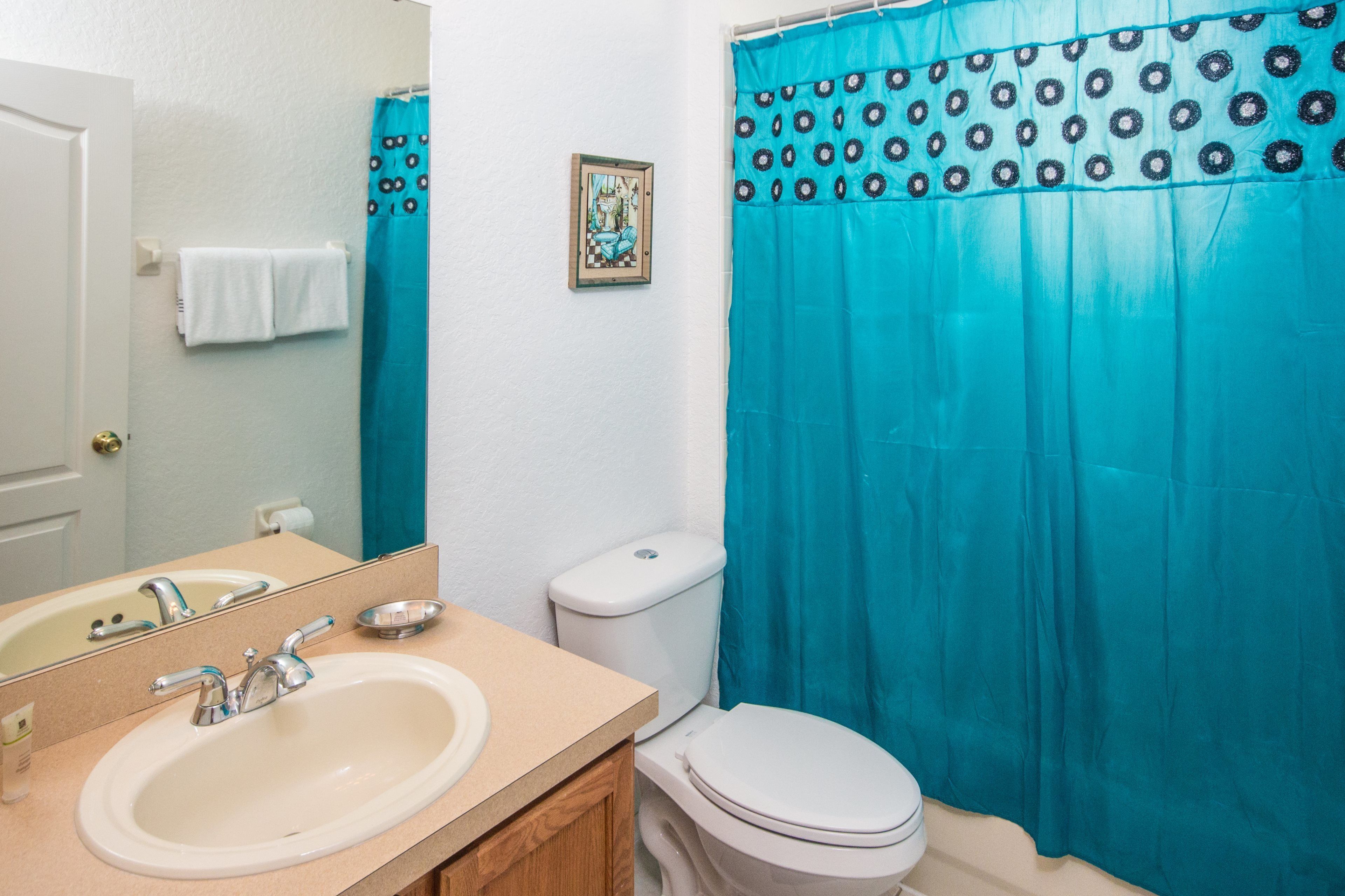 A bathroom with a sink, mirror, toilet, and a blue shower curtain with a circular pattern.