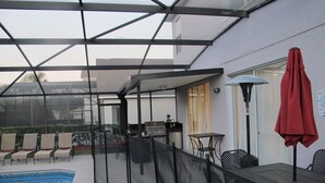 Un espacio al aire libre cubierto con piscina, sillas, mesa y una parrilla.