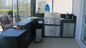 Cocina al aire libre con parrilla, pileta y zona de estar.