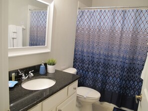 A bathroom with a white sink, a mirror above it, a toilet, and a shower curtain with a geometric pattern.
