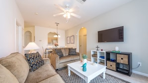 A living room with a sofa, coffee table, and a TV mounted on the wall. - Windsor Palms 2301 - 203 (Kissimmee)