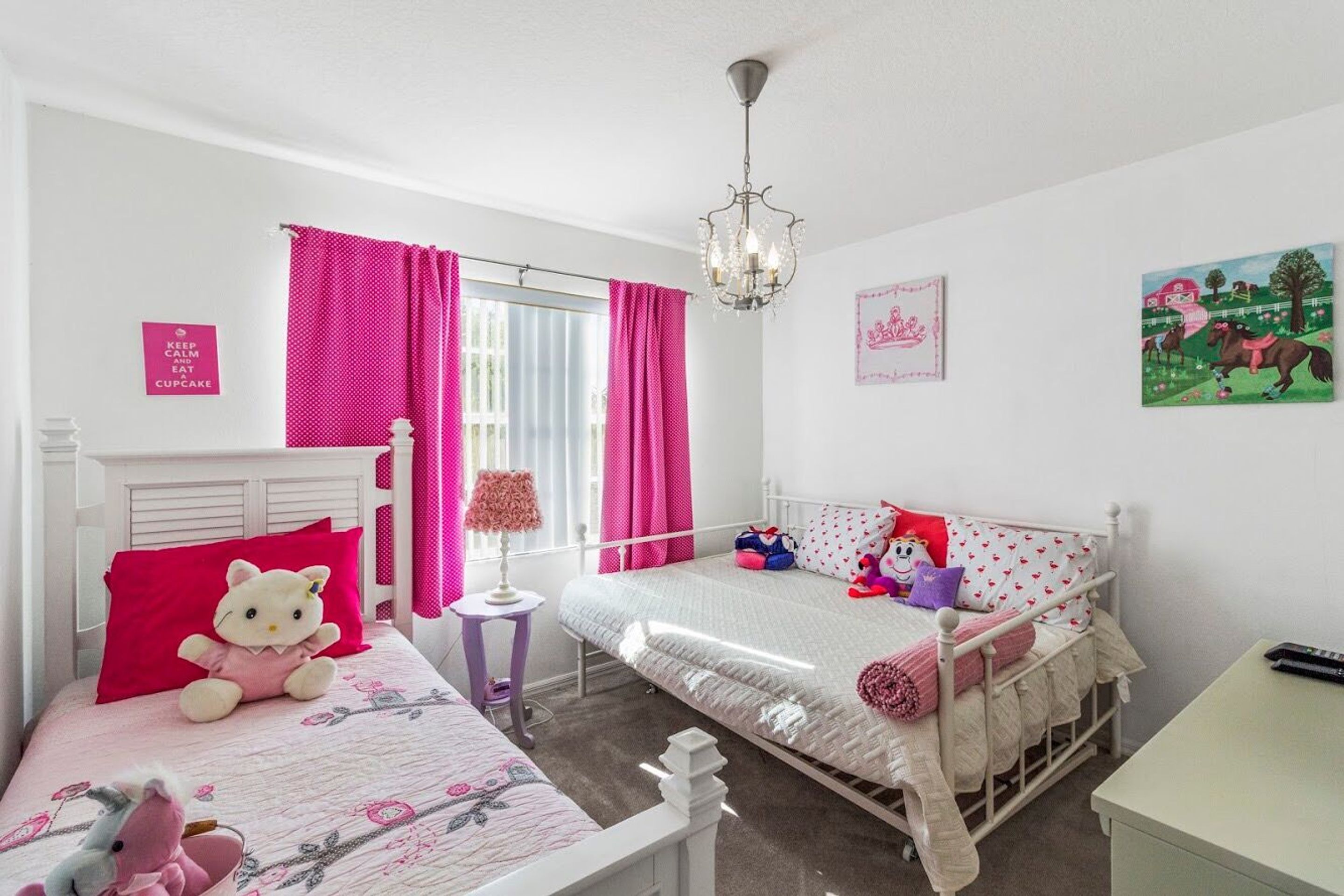 A child's bedroom with two beds, a chandelier, and a window with pink curtains.