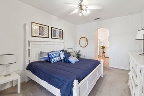 A bedroom with a white bed, a ceiling fan, a bedside table, a dresser, and a mirror. - Cumbrian Lakes 1204 (Kissimmee)
