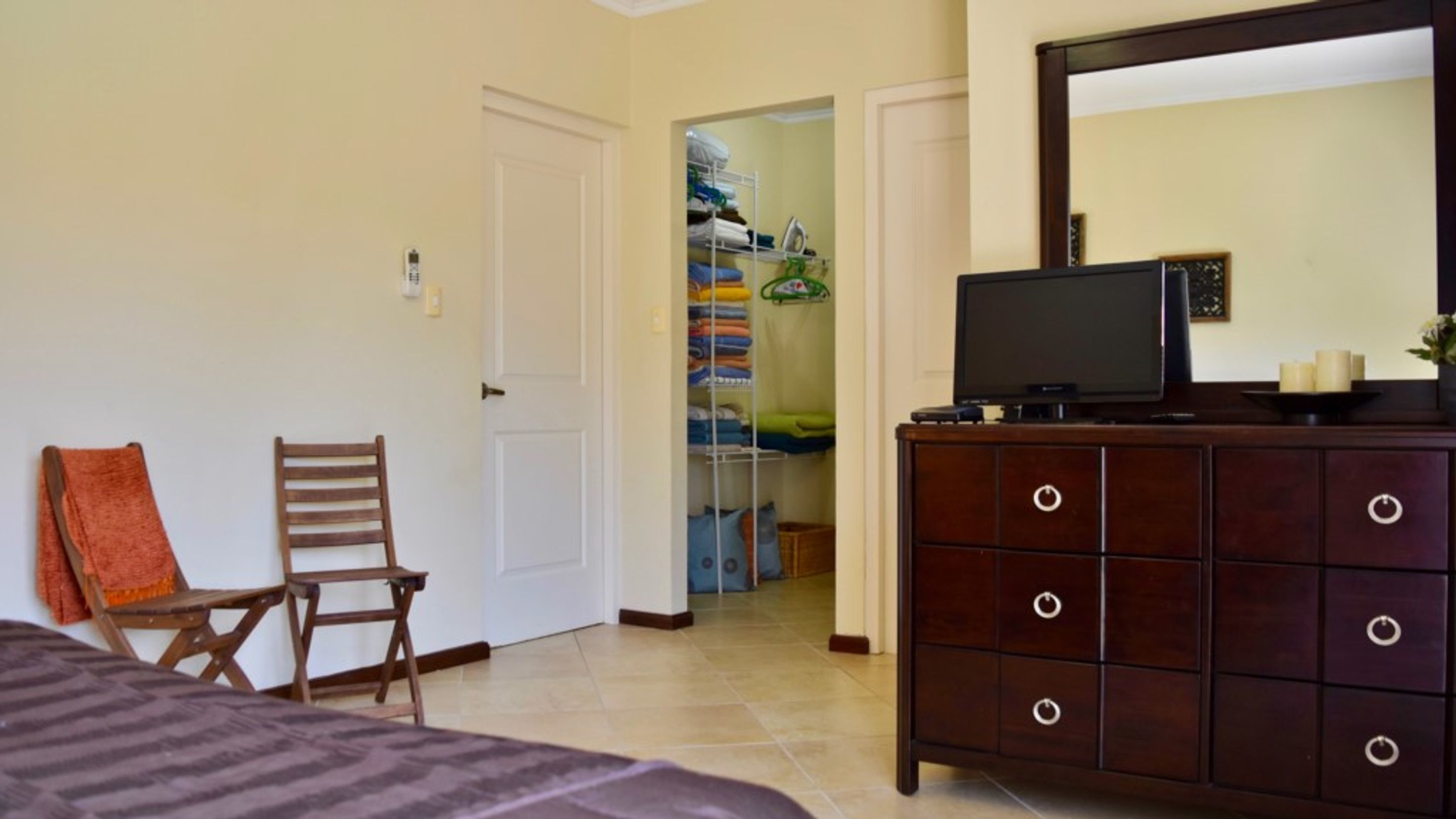 A bedroom with a bed, a wooden chair, a dresser with a mirror, and a closet with folded clothes.