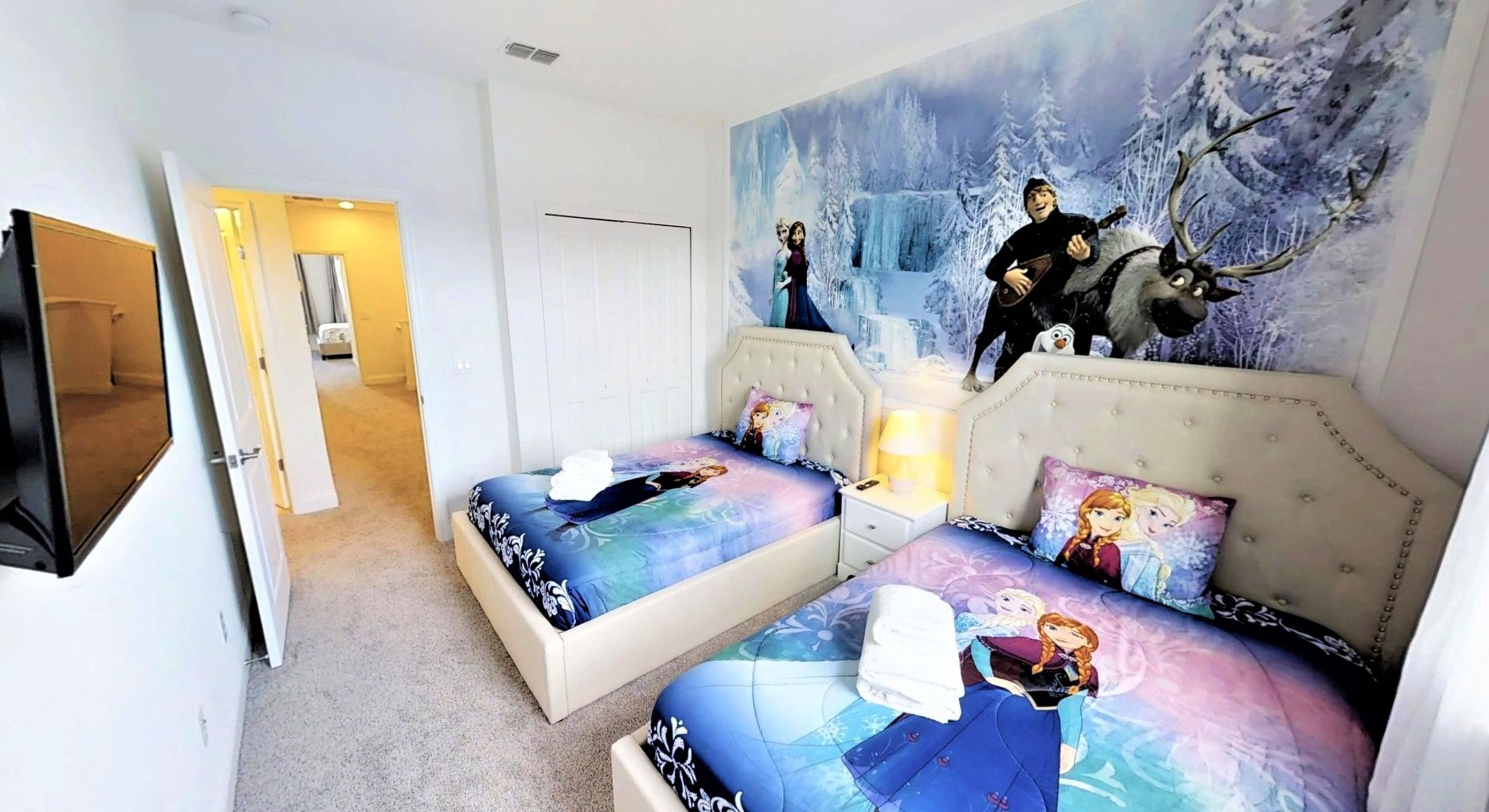 Une chambre avec deux lits, une fresque représentant un paysage hivernal et un téléviseur fixé au mur.