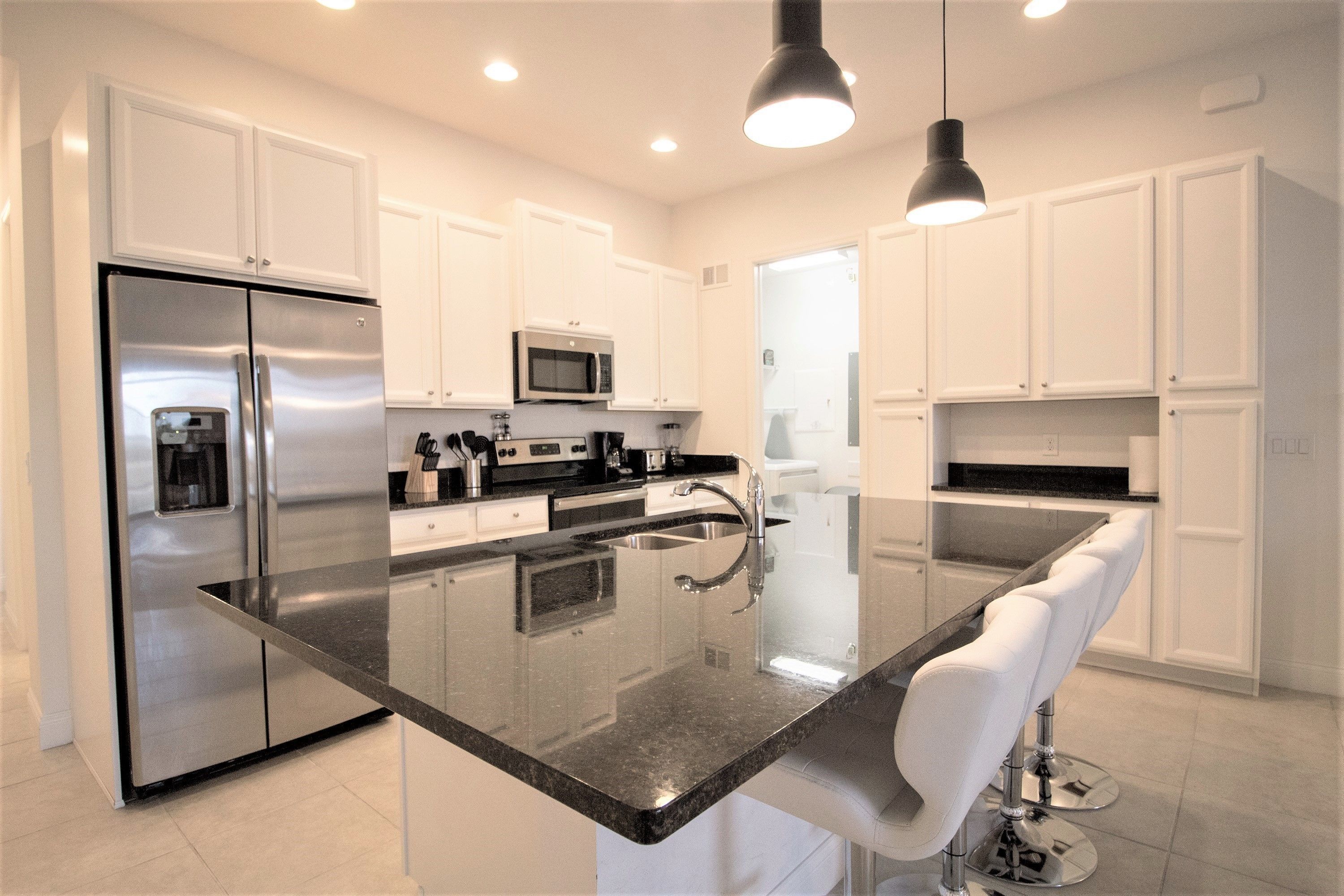 A modern kitchen with white cabinets, stainless steel appliances, a central island with seating, and pendant lighting.