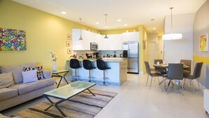 A modern living room with a sofa, coffee table, and dining area with chairs. - Serenity 17417 B (Clermont)