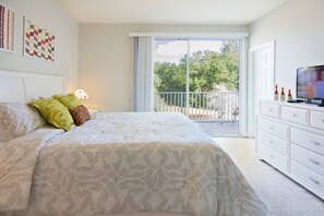 A bedroom with a large bed, a dresser, a television, and a balcony with a view of trees. - Serenity 17417 B (Clermont)