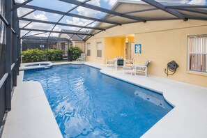 Piscina interior com teto de vidro, rodeada por espreguiçadeiras e uma pequena mesa.