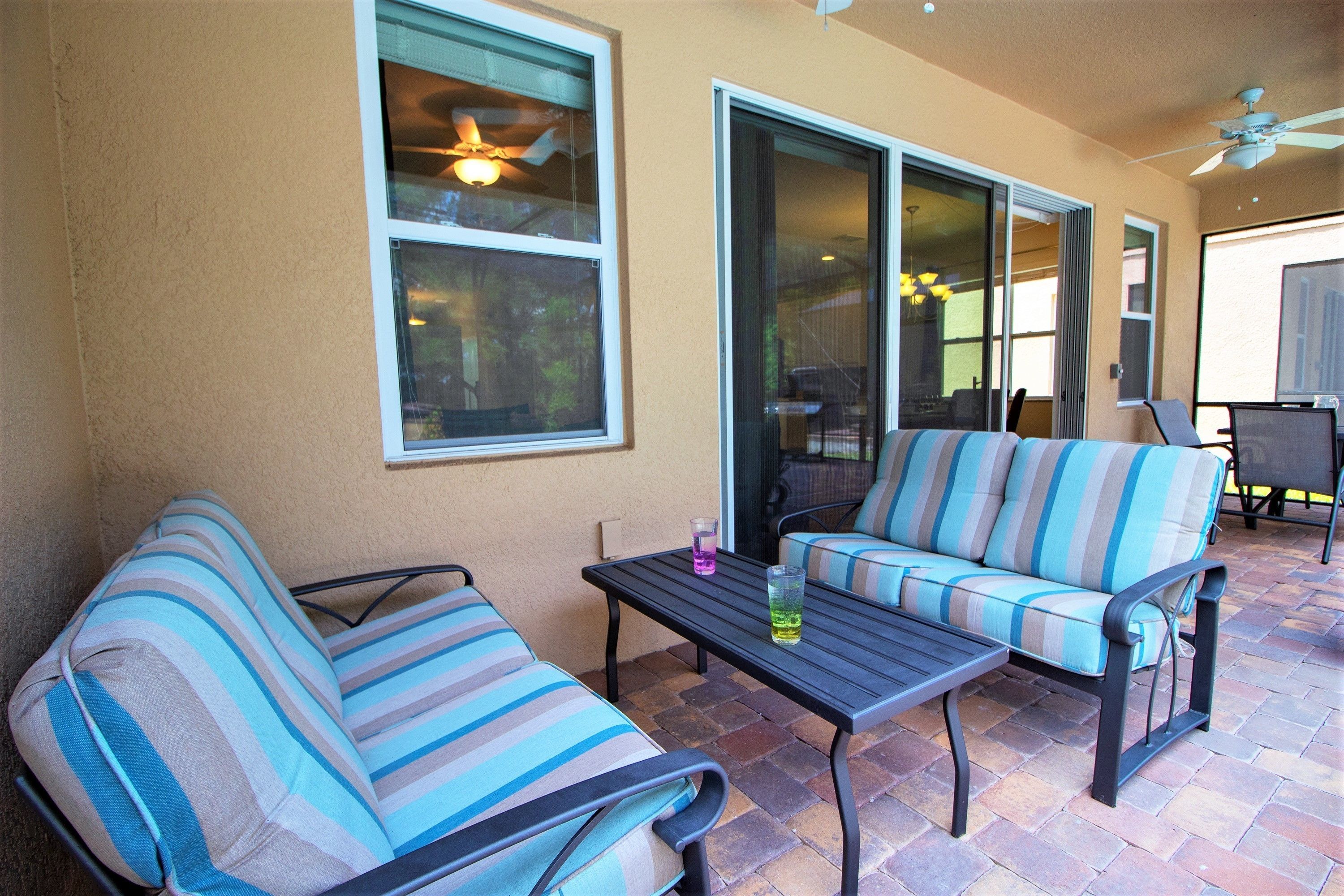 An outdoor patio area with striped sofas and a table, a ceiling fan, and a view through a glass door.