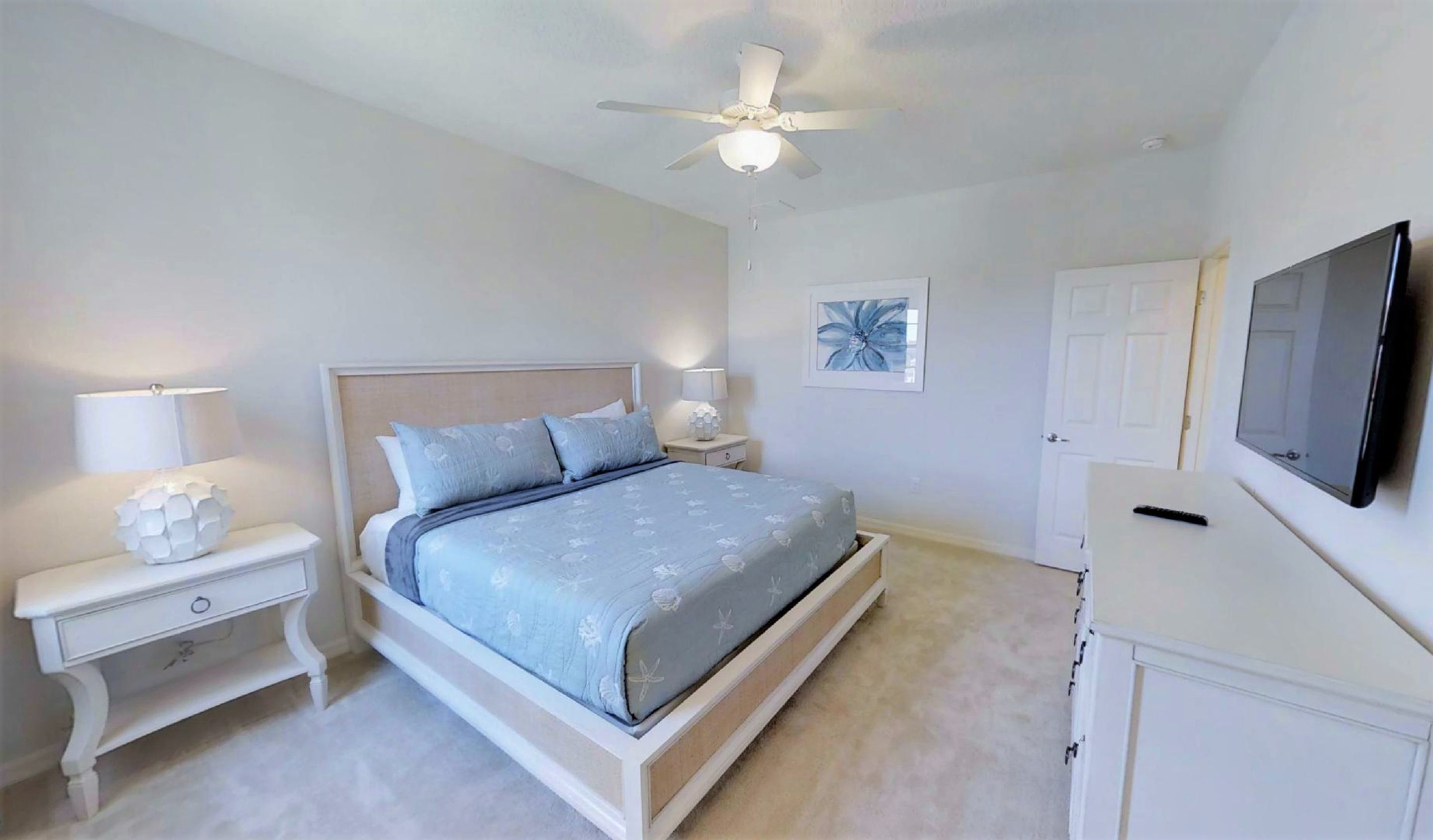 A bedroom with a bed, nightstands, a ceiling fan, a TV, and a door.