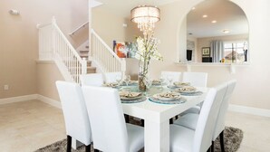 A dining room with a white table set for four, a chandelier, and a staircase leading to another level.