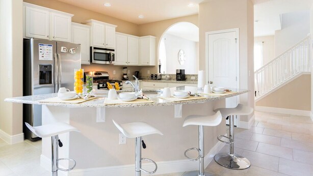 A modern kitchen with white cabinets, a stainless steel refrigerator, a microwave, and a large island with bar stools.