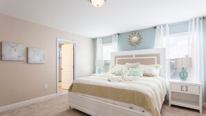 A bedroom with a bed, bedside tables, a door, and a wall with a sun decoration.