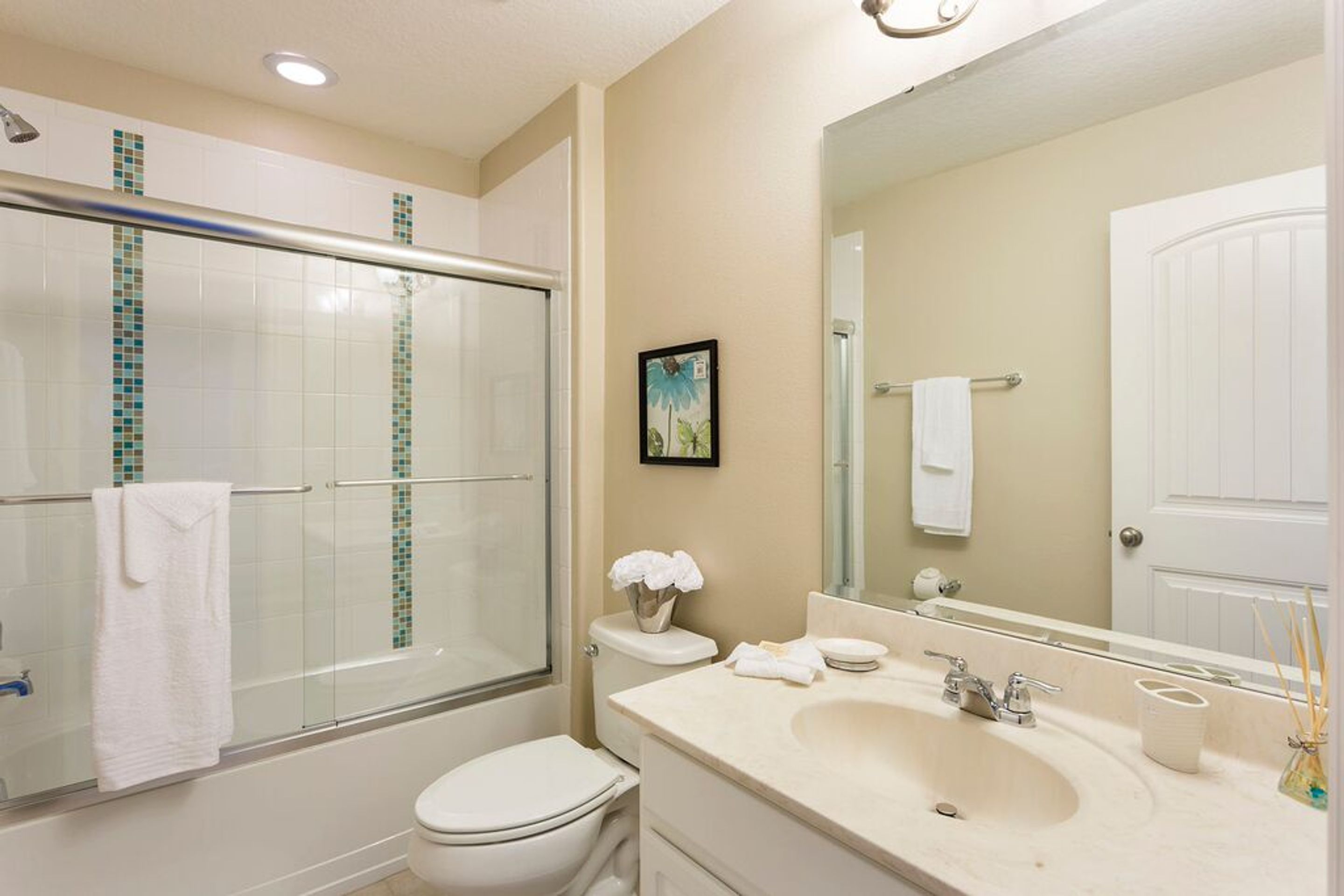 A bathroom with a glass-enclosed shower, a toilet, a sink with a mirror, and a framed picture on the wall.