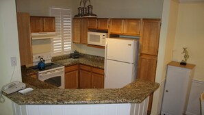 A compact kitchen with granite countertops, wooden cabinets, a microwave, a refrigerator, and a stove.