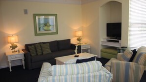 A living room with a sofa, armchairs, a coffee table, lamps, a television, and a framed picture on the wall.