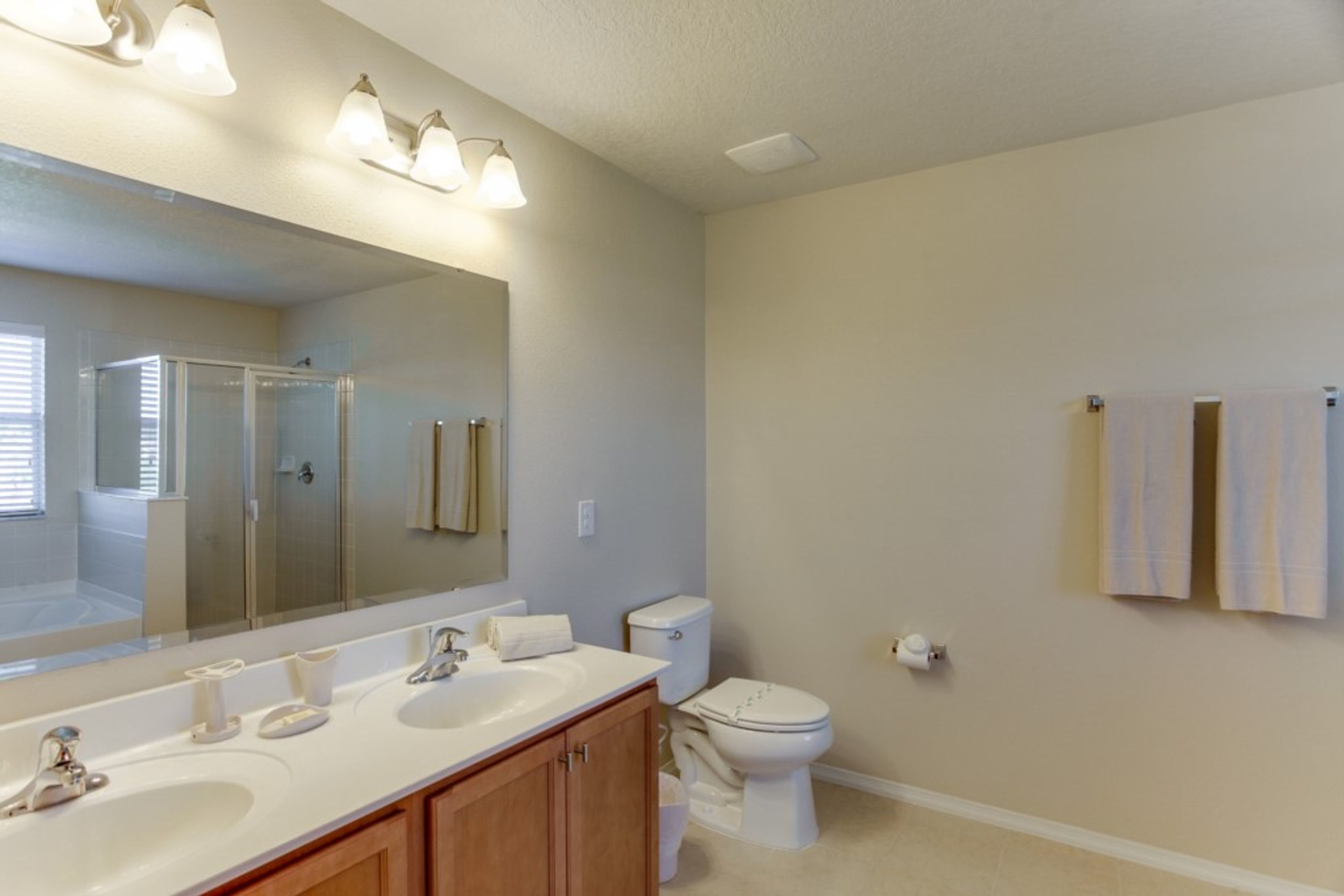 Une salle de bain avec un grand miroir, deux lavabos, des toilettes et une douche.