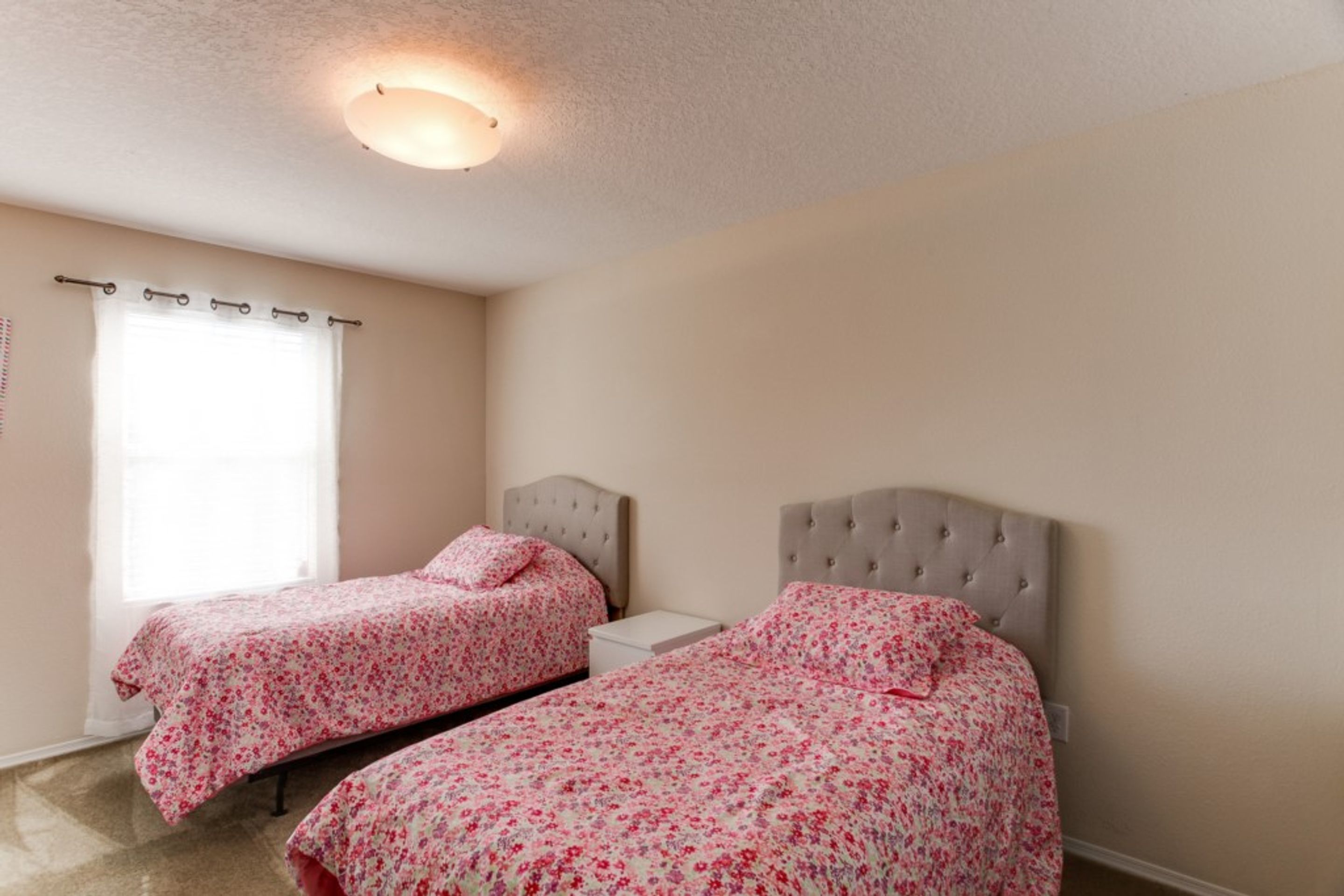 Une chambre avec deux lits, une fenêtre avec des rideaux et un luminaire au plafond.