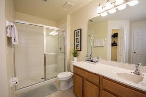 A bathroom with a glass-enclosed shower, a white toilet, a vanity with a sink, and a large mirror. - Bella Vida 480 (Kissimmee)