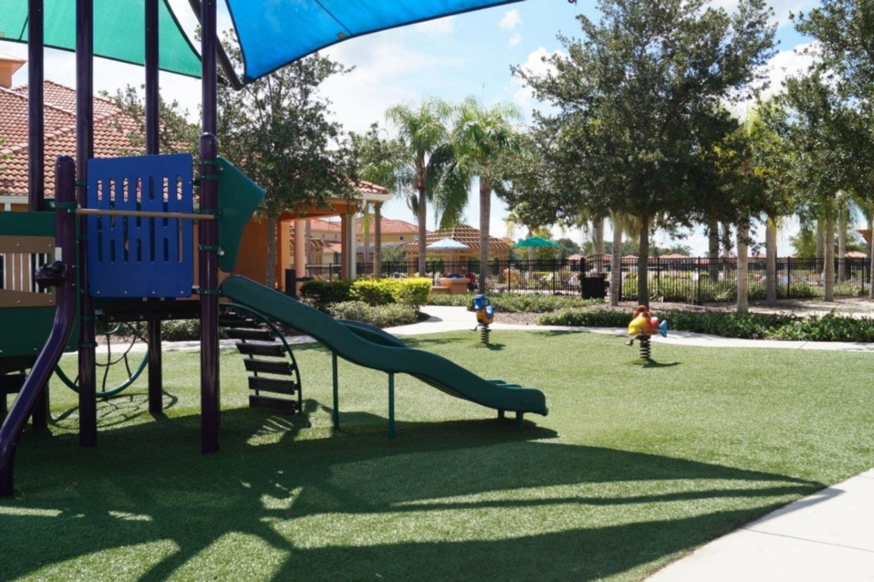 A playground with a slide and climbing structures, surrounded by trees and a fenced area.