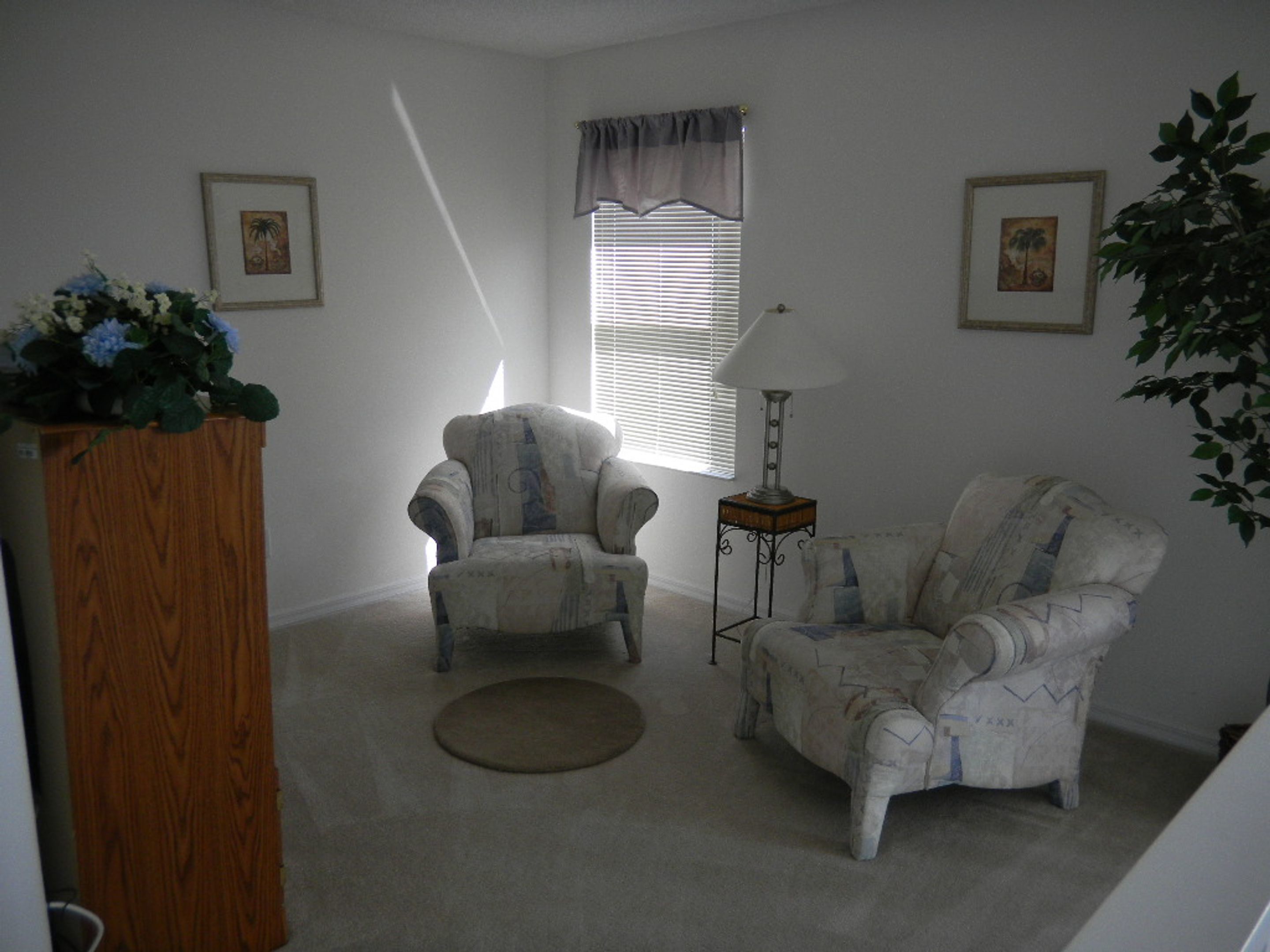 A living room with two armchairs, a wooden cabinet, a floor lamp, and a window with blinds.