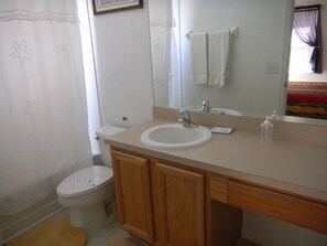 A bathroom with a white sink, wooden cabinets, a mirror, and a toilet.
