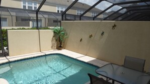A swimming pool with a glass enclosure, a small table, and a chair. - Windsor Hills 7677 (Kissimmee)