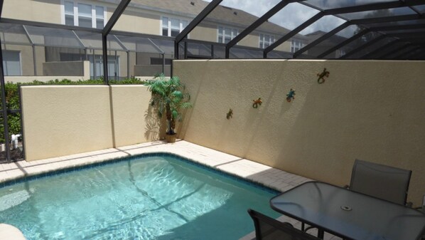 A swimming pool with a glass enclosure, a small table, and a chair. - Windsor Hills 7677 (Kissimmee)