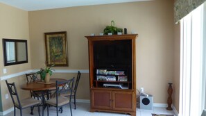 A dining area with a wooden table and chairs, a television stand with a flat-screen TV and a DVD player, and a potted plant. - Windsor Hills 7677 (Kissimmee)