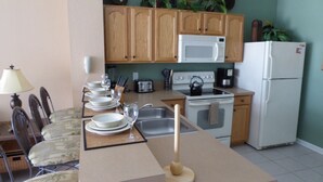 A compact kitchen with wooden cabinets, a microwave, a stove, and a refrigerator. - Windsor Hills 7677 (Kissimmee)