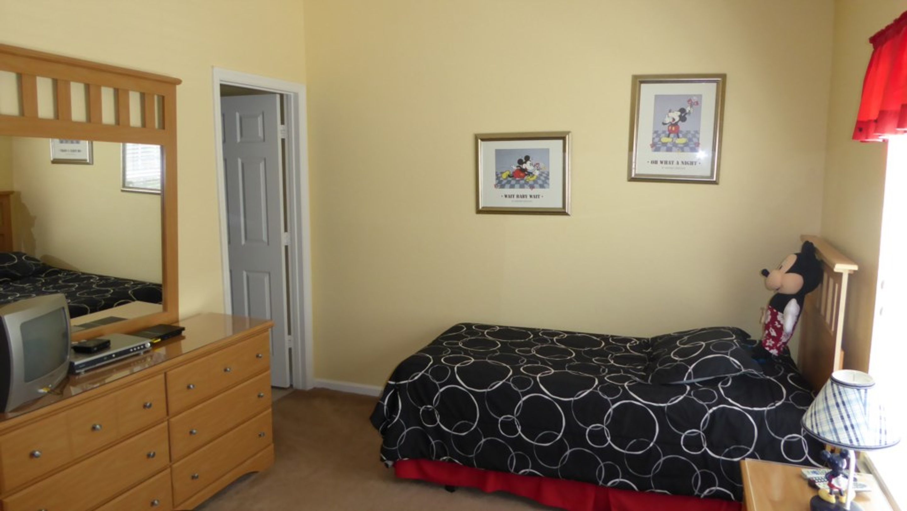 Une chambre à coucher avec un lit, une commode et un doudou à l’effigie de Mickey Mouse.