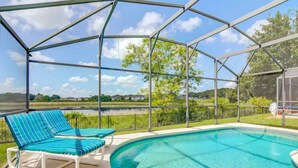 A covered outdoor swimming pool with two lounge chairs and a view of a lake and trees. - Southern Dunes 1120 (Haines City)